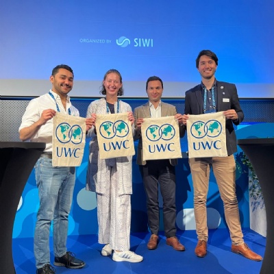 Four UWC graduates at an international event holding up UWC branded bags