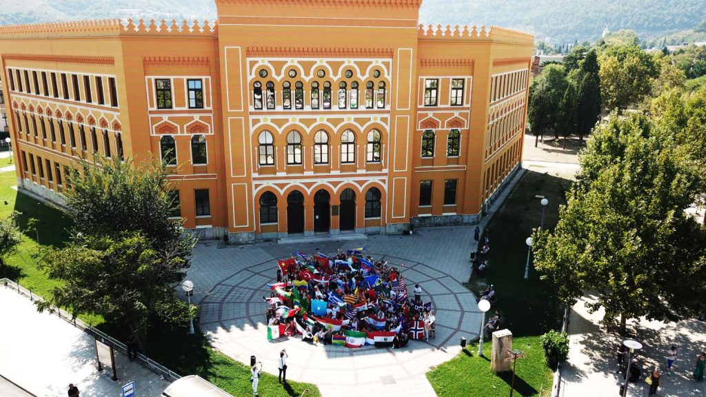 Aerial shot of students celebrating in front of campus building waving national flags